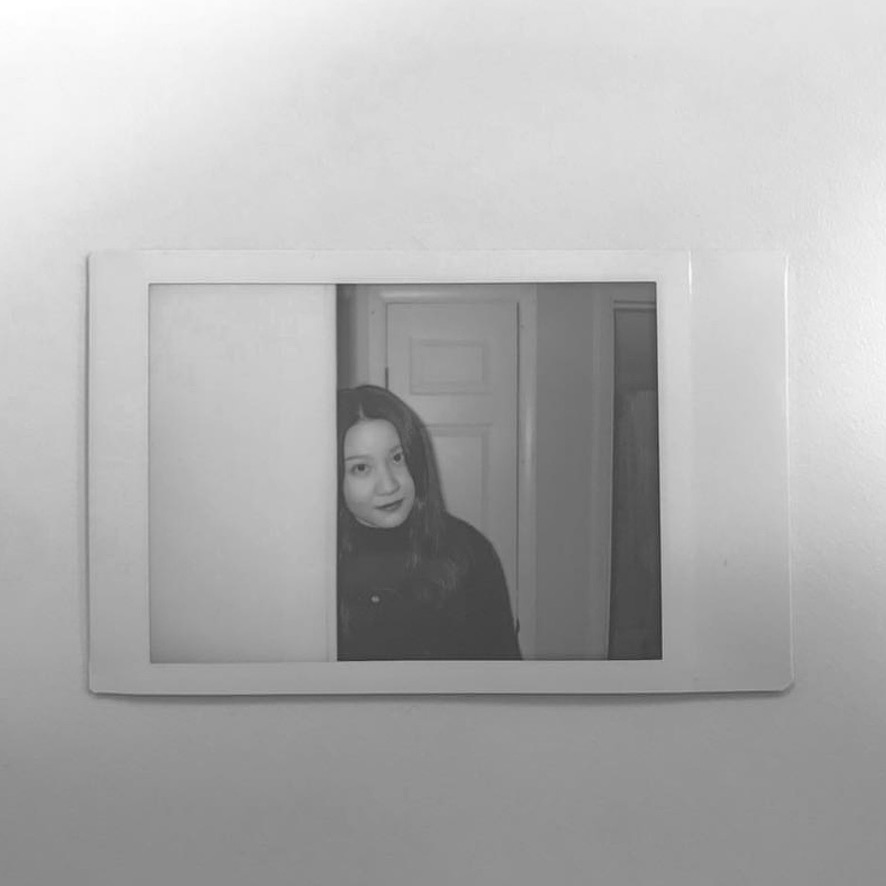 Sandra Shen, photographed in a rectangular mirror, in black and white.